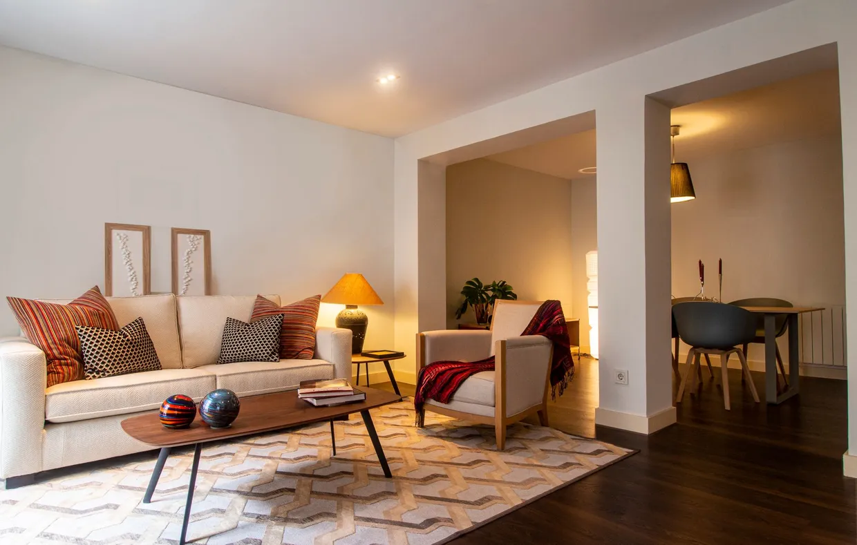 A warm, softly lit sitting room with a cream sofa, cushions, and a glowing lamp