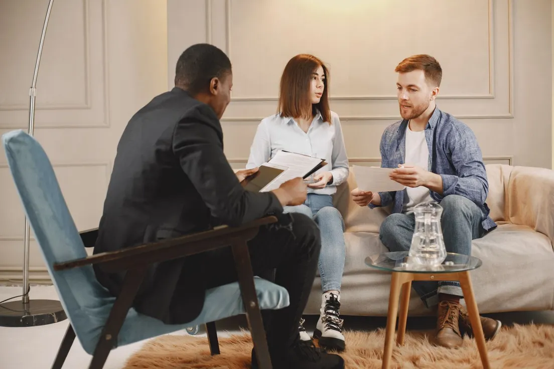 Three people talking together around a coffee table in a warm consultation room